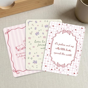 May include: Three decorative cards with whimsical designs. One card has pink stripes and a quote about books. Another features floral and bow patterns with the text "born to forced war." The third card has a heart pattern and a quote about books.