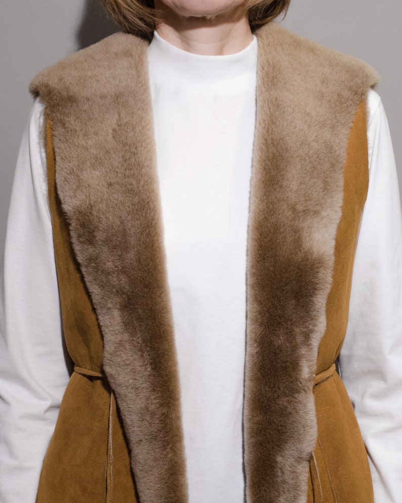 May include: A brown suede vest with a faux fur collar and a tie closure. The vest is lined with a soft, brown faux fur.