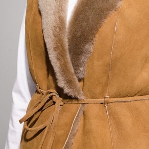 May include: A brown suede vest with a faux fur collar and a tie belt. The vest has a long, flowing style and is perfect for layering.