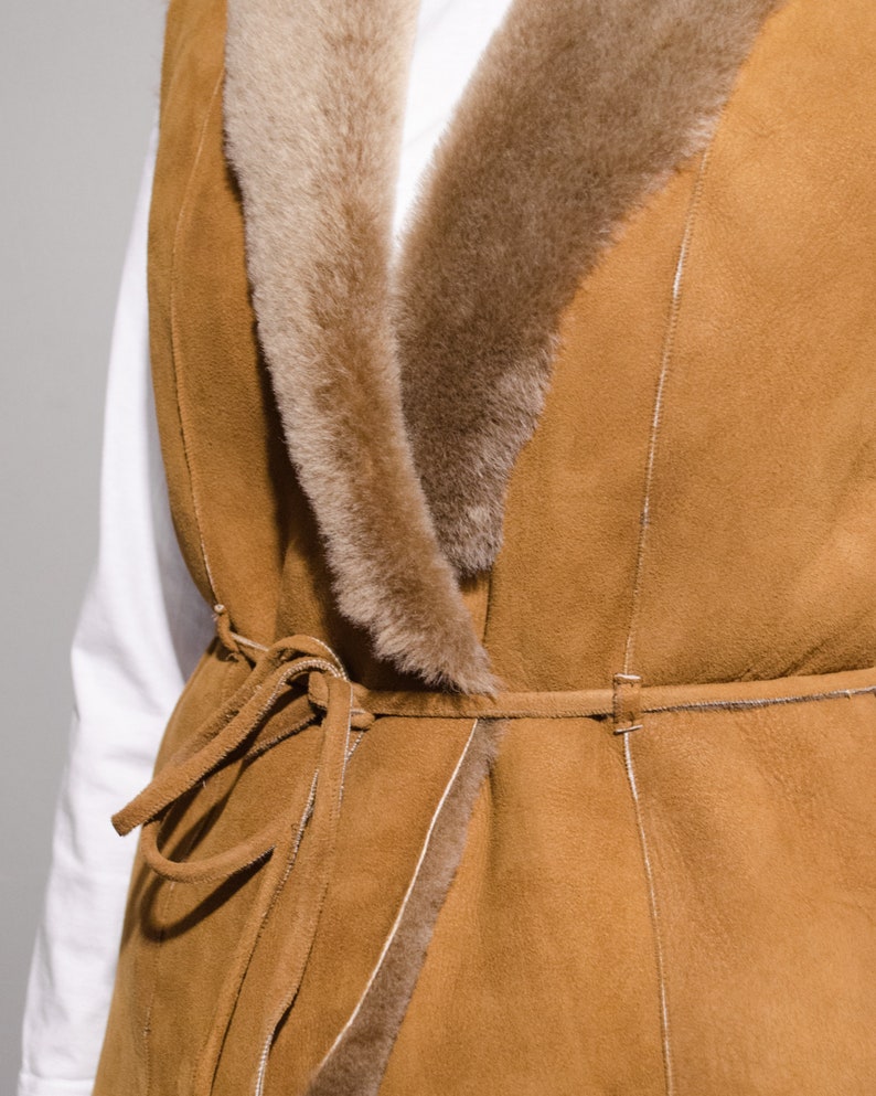 May include: A brown suede vest with a faux fur collar and a tie belt. The vest has a long, flowing style and is perfect for layering.