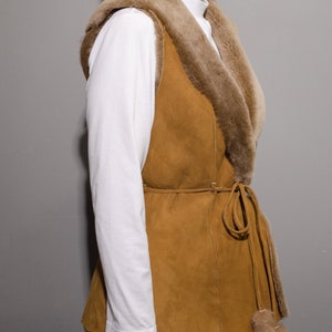 May include: A brown suede vest with a fur collar and a tie belt. The vest has a long, flowing style and is perfect for layering.