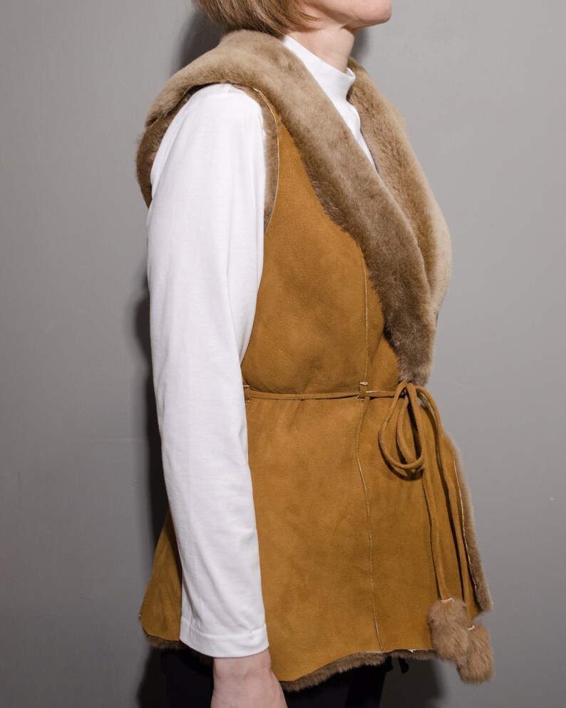 May include: A brown suede vest with a fur collar and a tie belt. The vest has a long, flowing style and is perfect for layering.