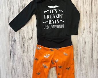 Może przedstawiać: Czarno-pomarańczowy strój dla niemowlęcia z nadrukiem nietoperza. Body ma napis "It's Freakin' Bats I Love Halloween".