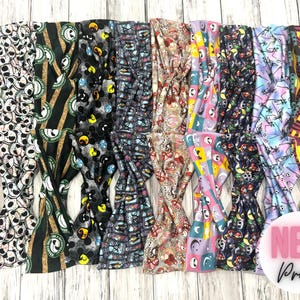 May include: A collection of colorful headbands with various patterns, including a black and white skull design, a green and gold striped design, a black and white Mickey Mouse design, a blue and white floral design, a red and white paisley design, a purple and yellow geometric design, a blue and white floral design, a pink and yellow geometric design, a black and white skull design, and a purple and yellow geometric design. The headbands are arranged in a row and are all tied in a knot. The text "NEW Prints" is visible in the lower right corner of the image.