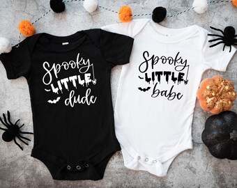May include: Two black and white baby onesies with Halloween-themed text. The onesie on the left says "Spooky Little Dude" and the onesie on the right says "Spooky Little Babe".