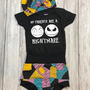 May include: A black baby outfit set featuring a headband, short-sleeved bodysuit, and shorts. The bodysuit has the text "MY PARENTS ARE A NIGHTMARE" with Jack and Sally faces. The shorts and headband have a patchwork design with yellow, teal, and purple.
