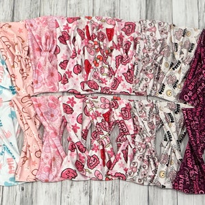 May include: A collection of 12 pink and white patterned headbands with various designs, including flowers, hearts, and text. The headbands are made of a soft, stretchy fabric and are perfect for adding a touch of style to any outfit.