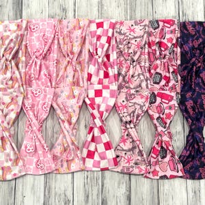 May include: Six pink and white patterned headbands with a pink and white checkered headband, a pink headband with a pink and white unicorn pattern, a pink headband with a pink and white Barbie logo pattern, a pink headband with a pink and white palm tree pattern, a pink headband with a pink and white makeup pattern, and a purple headband with a pink and purple Barbie logo pattern.