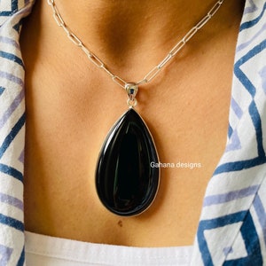 May include: A silver chain necklace with a large black teardrop pendant. The pendant is made of a smooth, polished stone.