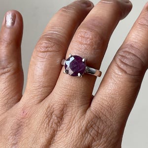 May include: A silver ring with a large, round, dark red gemstone set in a prong setting.