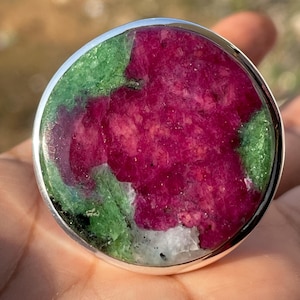 May include: A round, silver ring featuring a green and pink gemstone. The gemstone is a blend of green and pink, with a white centre.