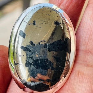 May include: A silver ring with a large oval-shaped pyrite gemstone. The pyrite has a metallic sheen and a black and gold color.