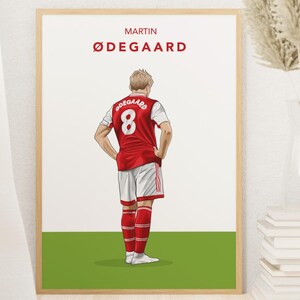 May include: A digital illustration of a soccer player wearing a red and white jersey with the number 8 on the back. The player is standing on a green field with the text "MARTIN ØDEGAARD" above him.