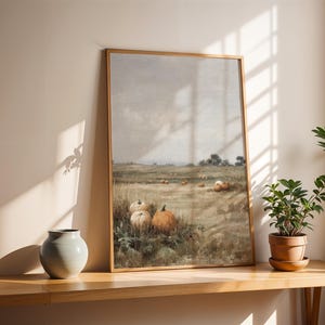 Puede incluir: Una lámina de arte enmarcada rectangular que presenta un paisaje de un campo con varias calabazas en primer plano. La escena muestra un cielo nublado y apagado sobre una pradera con calabazas naranjas y blancas dispersas a lo lejos.