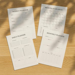 Könnte beinhalten: Vier weiße Papierplaner mit schwarzem Text auf einer Holzoberfläche. Die Planer umfassen einen Wochen-, Monats- und Tagesplaner sowie einen Monatskalender. Die Planer haben Abschnitte für Notizen, To-Do-Listen und Termine.