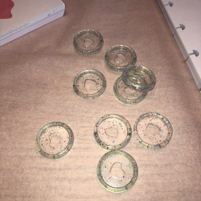 May include: Eight clear plastic binder clips with a heart-shaped cutout and glitter embedded in the plastic.