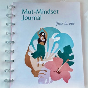 May include: A white journal with a blue, green, and pink floral design. The journal has a title that reads "Mut-Mindset Journal" and the text "Vive la vie" in a light purple font.