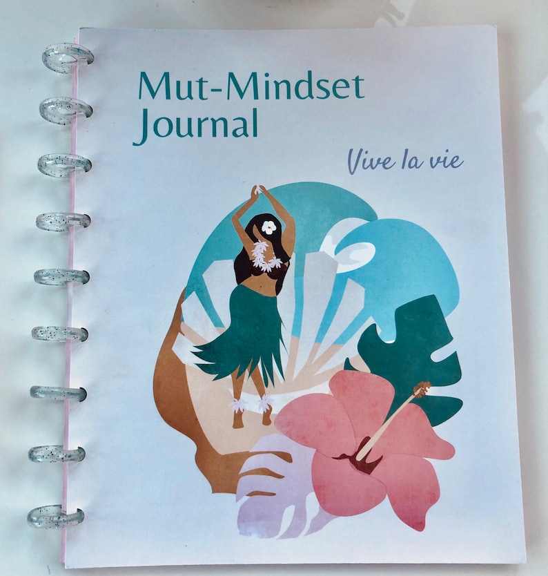 May include: A white journal with a blue, green, and pink floral design. The journal has a title that reads "Mut-Mindset Journal" and the text "Vive la vie" in a light purple font.