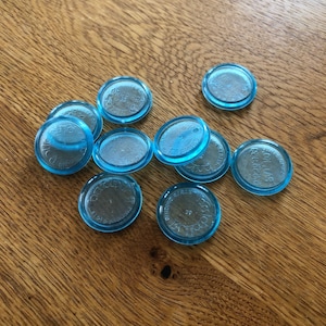 May include: A collection of clear, round tokens with a light blue rim and a silver center. The tokens are scattered on a wooden surface. The text on the tokens is blurry.