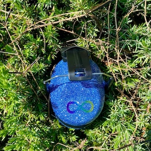 May include: Blue earmuffs with a rainbow infinity symbol on the front. The earmuffs are covered in glitter.