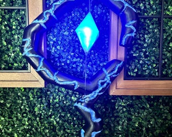Puede incluir: Un bastón negro con una gran sección superior abierta de forma hexagonal y un cristal azul brillante en forma de diamante suspendido en el centro. El bastón está decorado con patrones azules en relieve que recuerdan a rayos a lo largo.