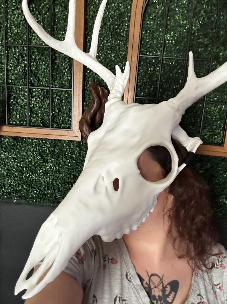 May include: A white deer skull mask with large antlers. The mask has eye and nose openings. The antlers are a bright white color. The skull is a matte white color. The mask is a costume or decorative item.