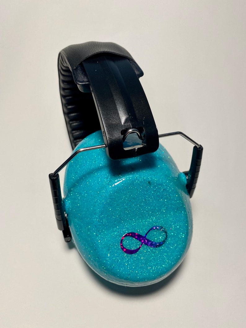 May include: Turquoise blue earmuffs with a black headband and an infinity symbol design. The earmuffs are covered in glitter.