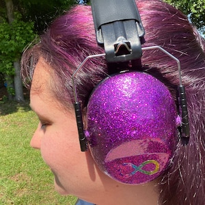 May include: Purple earmuffs with a rainbow infinity symbol on the side. The earmuffs are covered in glitter.