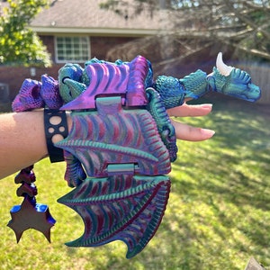 May include: A iridescent purple and green dragon toy with articulated wings and a white horn. The dragon is made of plastic and has a detailed design.