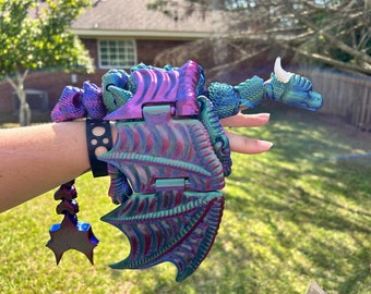 May include: A iridescent purple and green dragon toy with articulated wings and a white horn. The dragon is made of plastic and has a detailed design.