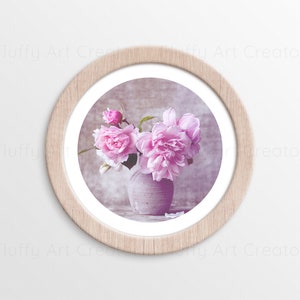 May include: A framed photograph of a bouquet of pink peonies in a light gray vase. The flowers are arranged in a cluster and the vase is sitting on a textured surface.