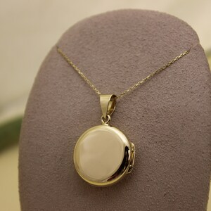 Puede incluir: Un collar con un colgante de medall&oacute;n redondo dorado. El colgante tiene forma circular pulida con una apertura con bisagras. La cadena es delicada y tambi&eacute;n dorada. El medall&oacute;n se exhibe sobre una superficie gris texturizada.