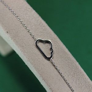 May include: A silver chain bracelet featuring a cloud-shaped pendant. The pendant is hollow and has a delicate design.