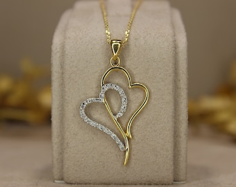 Può includere: Collana con pendente dorato con design a doppio cuore. Un cuore è dorato, l'altro è incastonato con piccole pietre trasparenti. La collana è appesa a una sottile catena d'oro. Un gioiello elegante.