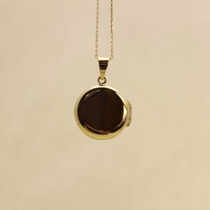 Puede incluir: Un collar con un medall&oacute;n dorado redondo. El colgante es de color oro brillante y reflectante, colgado de una delicada cadena. El medall&oacute;n est&aacute; cerrado, sobre un fondo neutro.