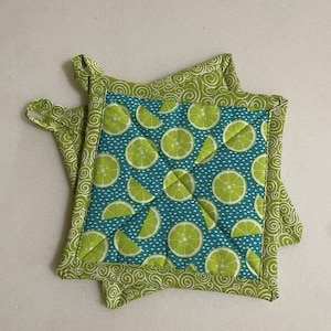 May include: Two green and blue quilted pot holders with a lime pattern. The pot holders have a green swirl pattern on the border.