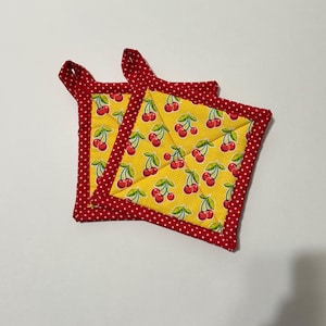 May include: Two red and yellow quilted pot holders with a cherry print. The pot holders have a red border with white polka dots.