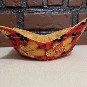 May include: A red and black plaid fabric bowl with gingerbread men designs. The bowl is lined with a tan fabric.