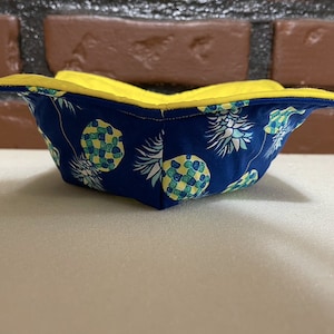 Könnte beinhalten: Eine gelbe und blaue Stoffschale mit Ananas-Muster. Die Schale ist zur Hälfte gefaltet und die Innenseite ist gelb.