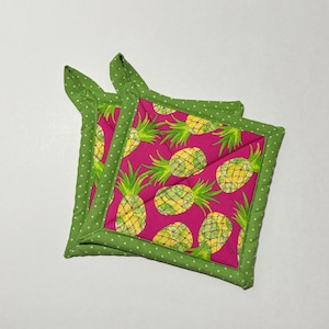 May include: Two green and white polka dot hot pads with a pink background and a pineapple pattern.