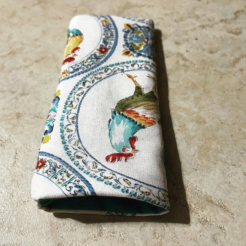 May include: A white fabric utensil holder with a teal lining. The fabric has a repeating pattern of blue, green, and yellow roosters in circular frames.