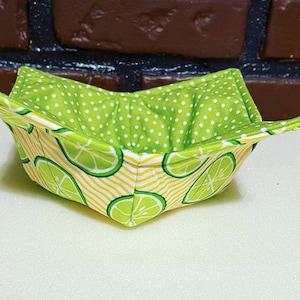 May include: A green and yellow fabric bowl with a lime pattern. The bowl is folded and has a white polka dot lining.
