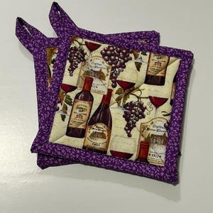 May include: Two purple quilted pot holders with a wine bottle and grape design. The pot holders have a purple border with a small white floral pattern.