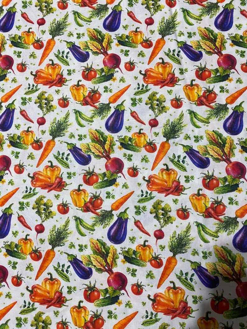 Op de afbeelding: Een witte stof met een herhalend patroon van kleurrijke groenten, waaronder oranje wortels, paarse aubergines, rode tomaten, gele en oranje paprika's, groene komkommers, rode radijsjes, groene erwten en groene kruiden.