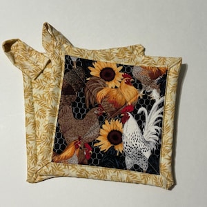 May include: Two square pot holders with a farm theme. The centre of each pot holder features a black background with images of chickens, sunflowers, and a chicken wire pattern. The edges and hanging loops are a light yellow fabric with a leaf pattern.