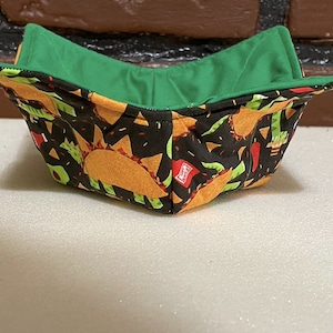 May include: A green and black fabric bowl with a taco pattern. The bowl is folded and has a green lining.