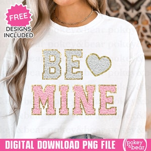 Peut inclure: Sweat-shirt blanc avec un motif en paillettes dorées qui dit "BE" avec un cœur en paillettes blanches et "MINE" en paillettes roses.
