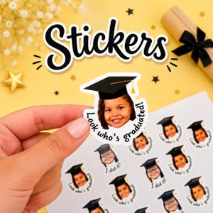 Può includere: Un adesivo personalizzato con la fotografia di un bambino che indossa un tocco di laurea nero. L'adesivo include il testo Look who's graduated in un carattere nero circolare. Il design è stampato su un foglio adesivo bianco con varie copie.