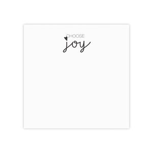 以下が含まれることがあります： 黒い文字で「CHOOSE joy」と書かれた白いカード。CHOOSEの上には小さな黒いハートマークがあります。