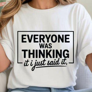 May include: White t-shirt with the text "EVERYONE WAS THINKING it i just said it," in a black rectangular box. The shirt has short sleeves.